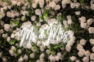 Neon "Mr &amp; Mrs" sign on a white rose flower wall.