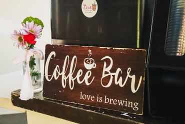 A cozy coffee bar sign with flowers and the phrase 'love is brewing'.