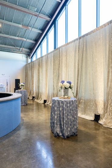 Elegant event space with high windows and floral-decorated cocktail tables.