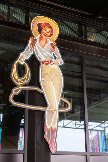 Vintage neon sign of a smiling cowgirl with a lasso.