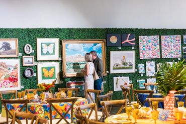 A couple admires art on a green wall in a colorful, festive setting.