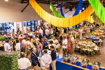 A busy indoor social event with colorful decorations and buffet tables.