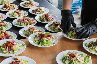Multiple plates of fresh salad being prepared by a person wearing black gloves.