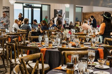 Guests enjoy a lively dining event in a warmly decorated room with wooden chairs and orange table runners.
