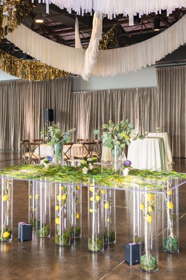 Transparent table with lemons and greenery under elegant white and gold ceiling decorations.