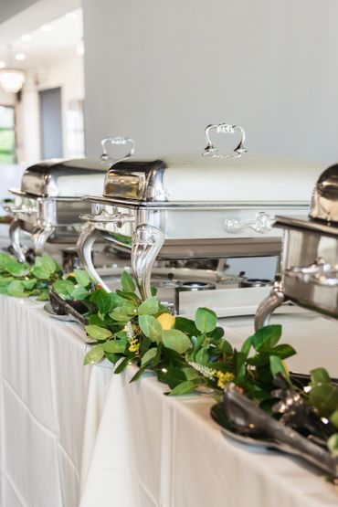 Elegant buffet setup with silver chafing dishes and greenery decor.
