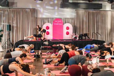 A large group participating in a fitness or yoga class in a spacious hall.