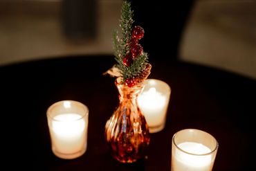 Three lit candles and a festive vase with pine and berries on a dark surface.
