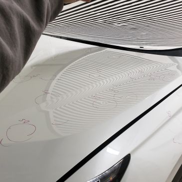 Reflections of a striped fabric on a white car hood.
