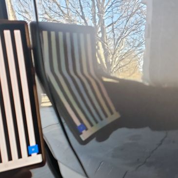 Reflection of striped panels on a shiny surface with trees in the background.