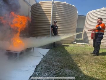 Person using a fire extinguisher to put out flames outdoors.