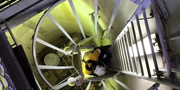 Worker in safety gear descends industrial spiral staircase.