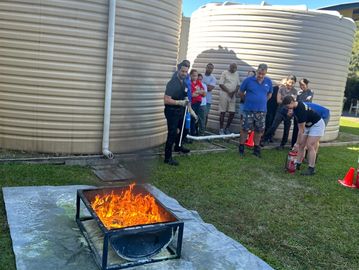 Group participating in a fire safety training with a controlled fire and fire extinguishers.