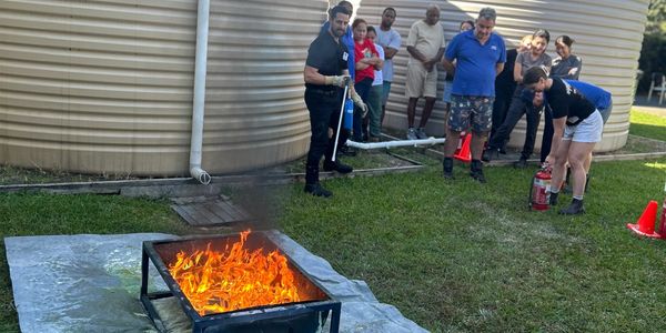 People practicing fire extinguisher use on a controlled fire outdoors.