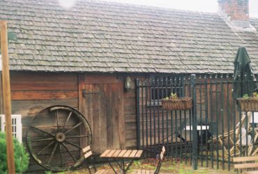 Rustic wooden shed with a large wagon wheel and metal gate.
