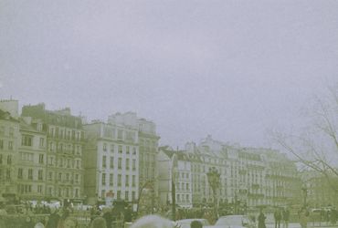 Historic buildings line a bustling city street under a grey sky.