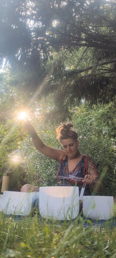 Woman playing crystal singing bowls outdoors at sunset.