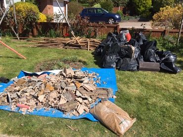 Black Bags Filled With Roof Tiles. And Loose Roof Tiles On Blue Sheet In Front Garden.