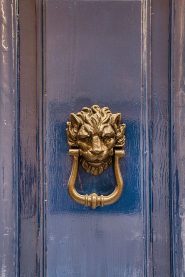 Antique brass lion head door knocker on a blue wooden door.