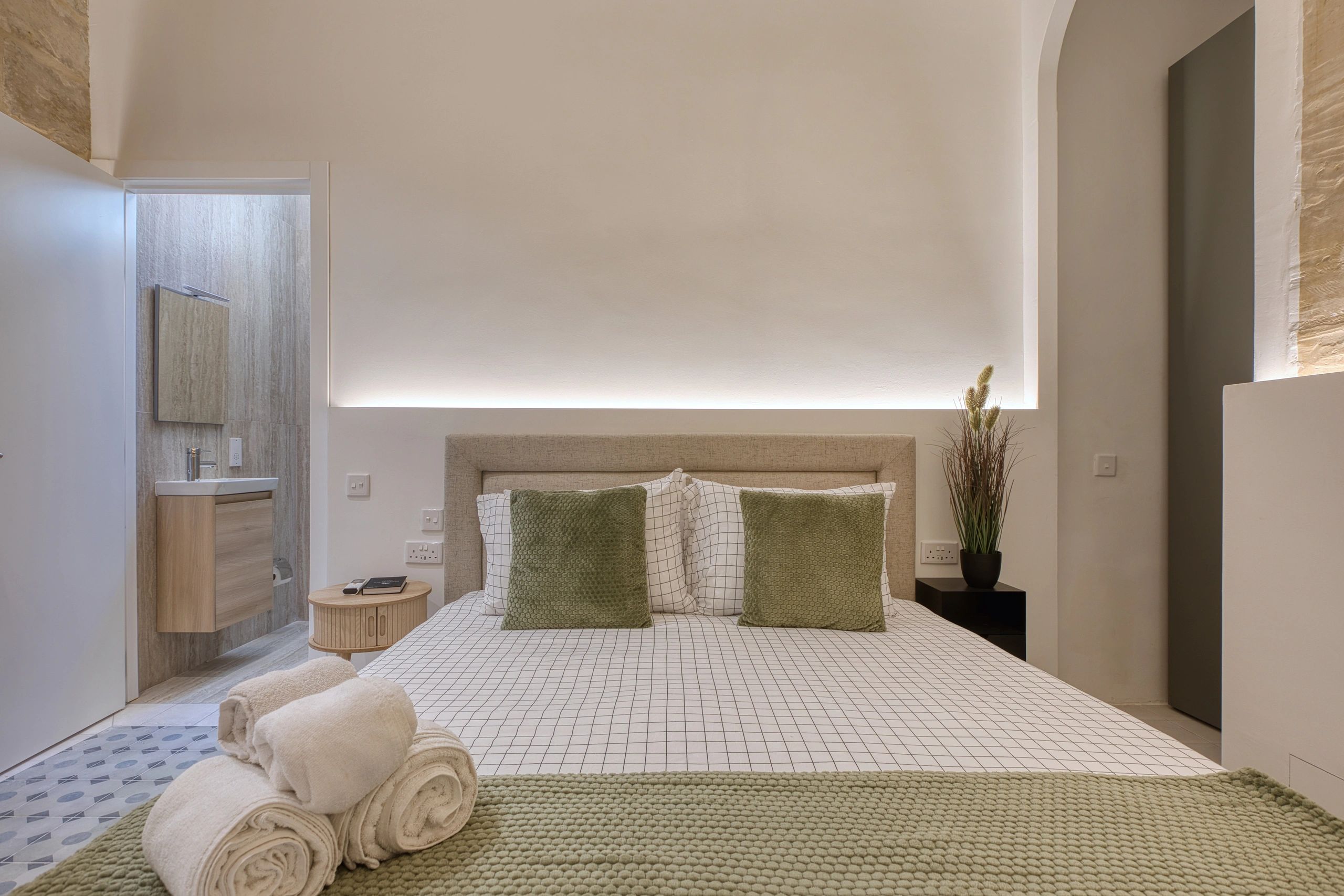Minimalist bedroom with a cozy bed, green accents, and soft lighting.