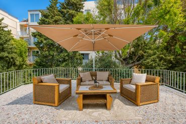 Outdoor patio furniture set with a large beige umbrella on a sunny day.