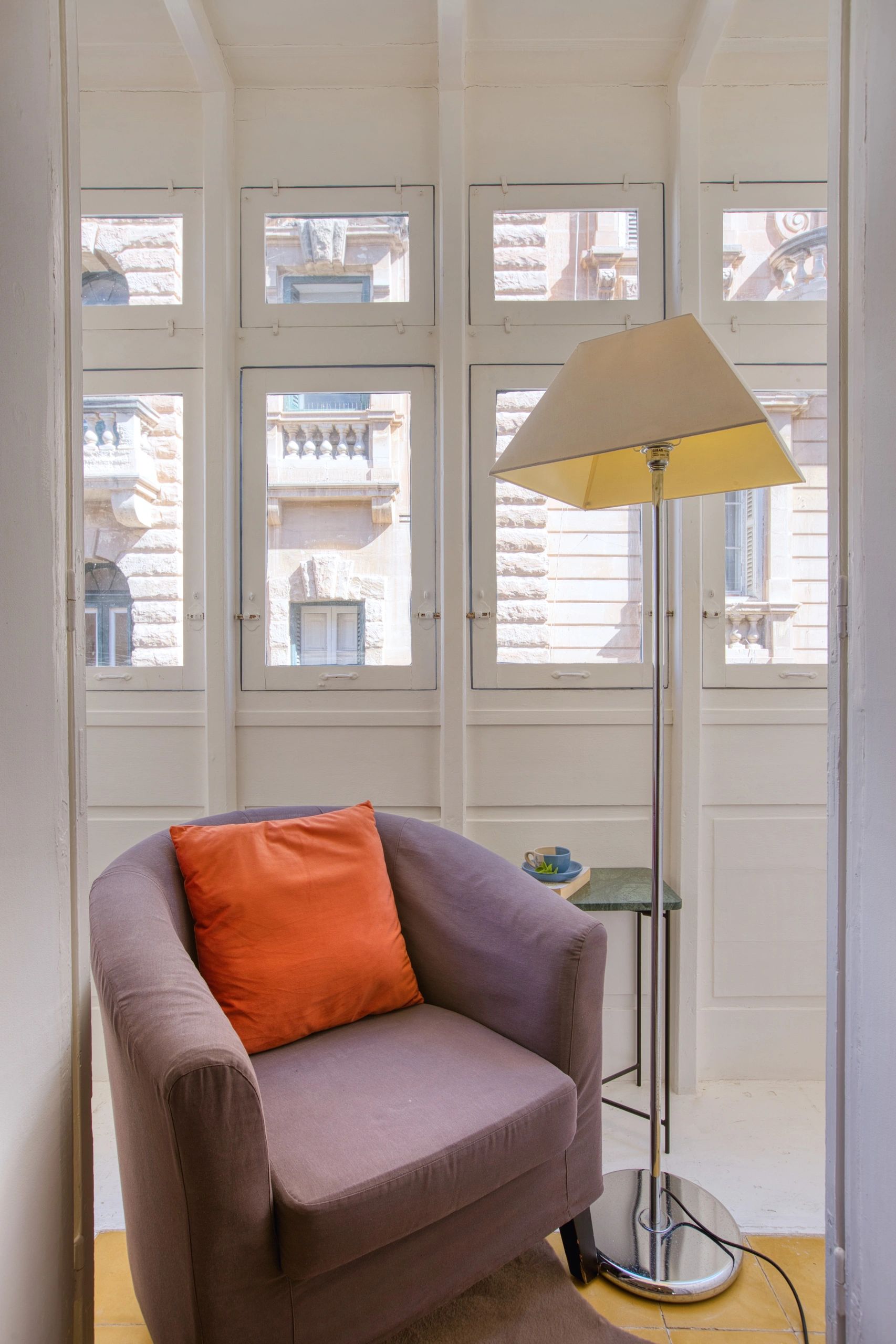 Cozy armchair with orange cushion near a modern floor lamp by tall windows.
