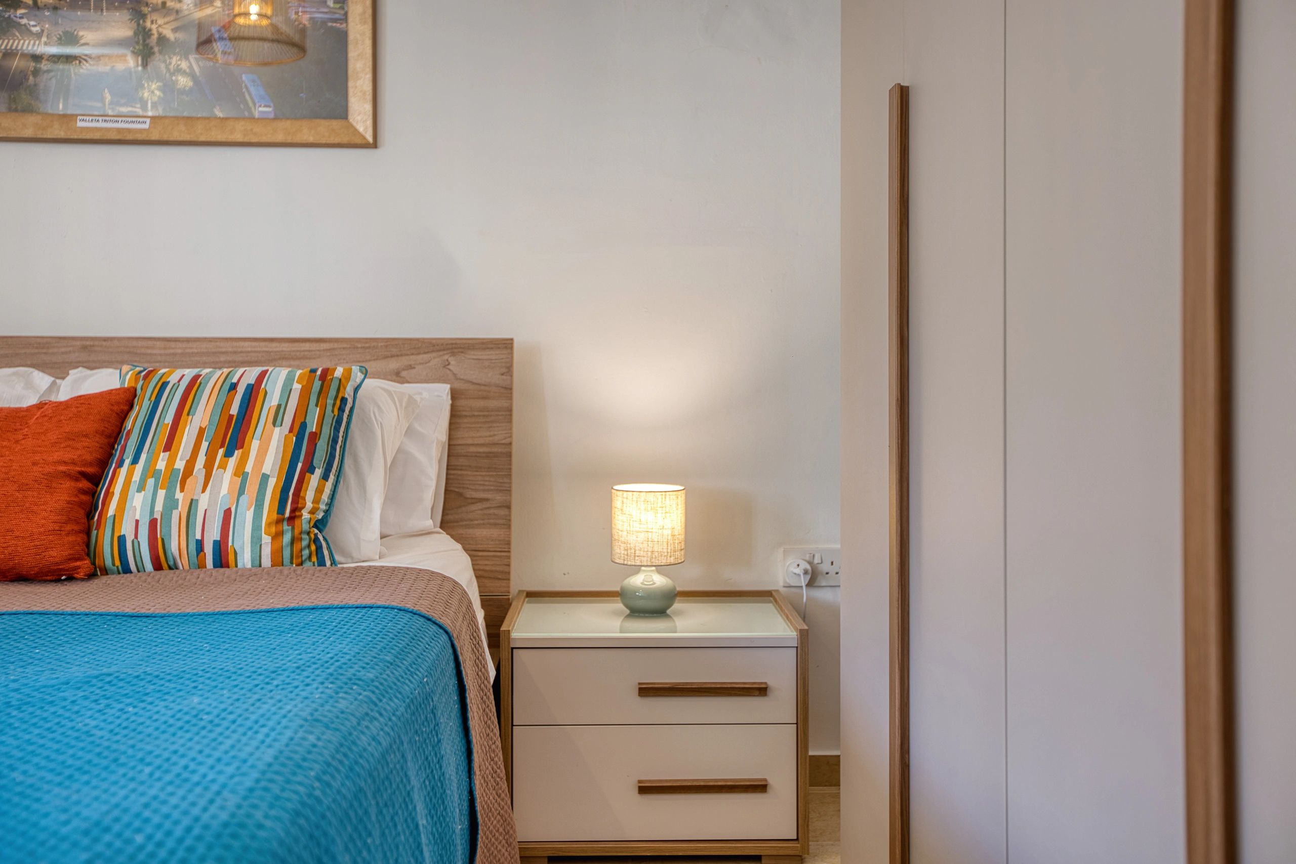 Cozy bedroom with colorful pillows and a bedside lamp.