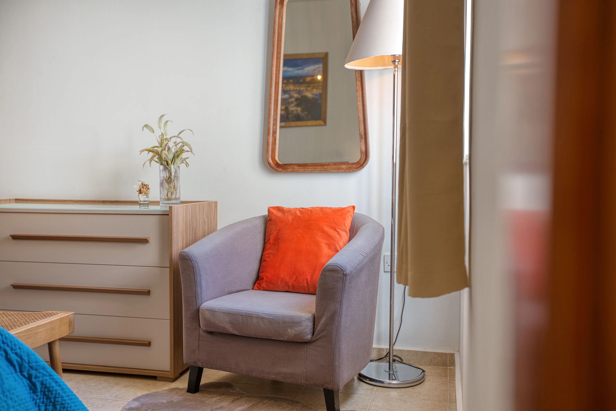 Cozy gray armchair with an orange pillow in a bright room corner.