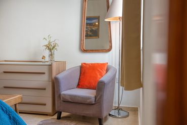 Cozy gray armchair with an orange pillow in a bright room corner.