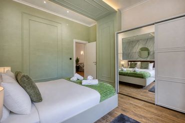 Modern bedroom with green accents and a mirrored wardrobe reflecting the bed.