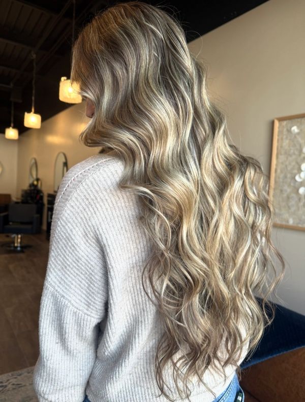 Long, wavy blonde hair with highlights styled beautifully indoors.