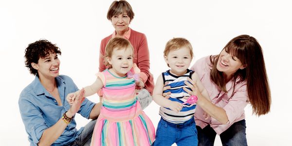 Three generations of women joyfully playing with two toddlers in a studio.