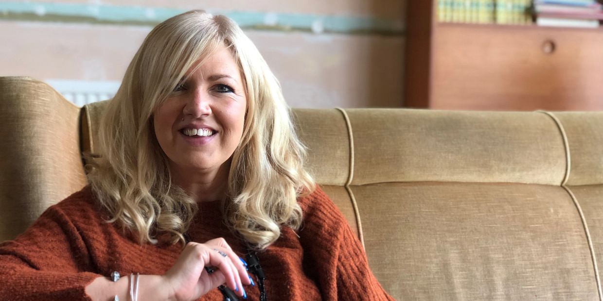 Woman with blonde hair sitting on a beige couch, smiling.
