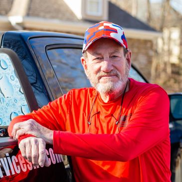 Man in red shirt and camo cap leaning on black vehicle outdoors.
