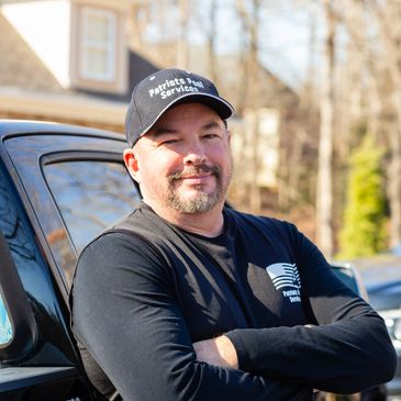 Man in black shirt and hat standing confidently by a vehicle outdoors.