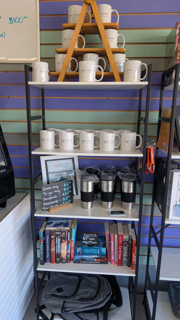 A retail shelf displays mugs, books, backpacks, and travel cups for sale.