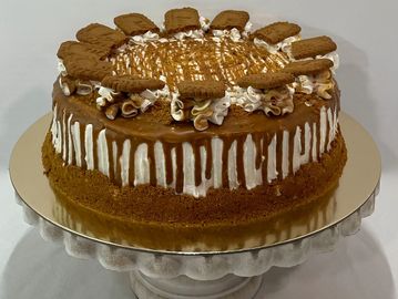 A caramel-drizzled cake topped with cookies on a white cake stand.