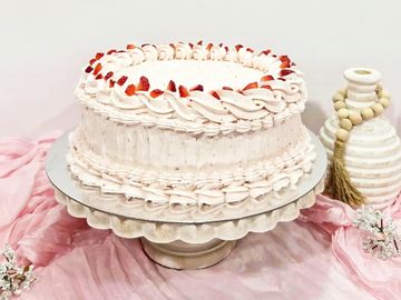 Elegant strawberry cream cake on a decorative stand with a soft pink cloth background.