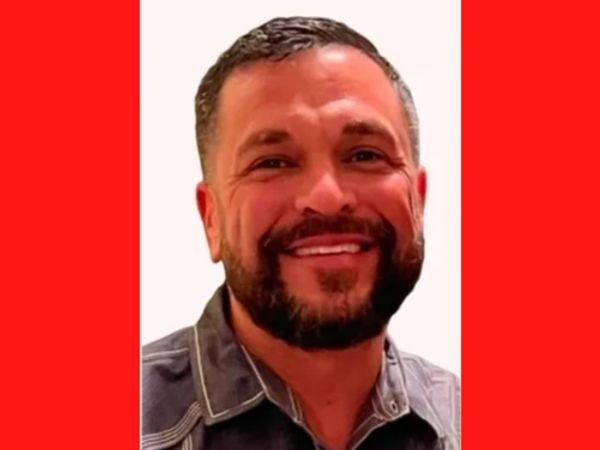Smiling man with beard against a red background.