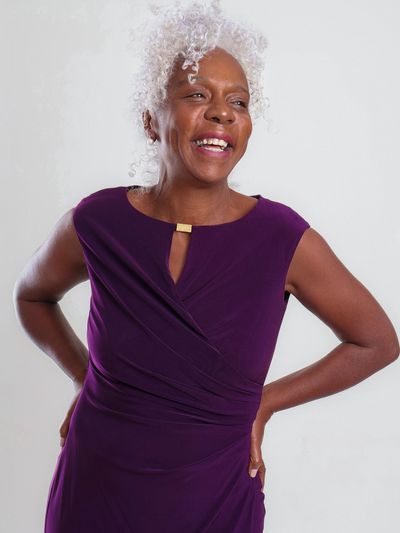 Smiling woman in a purple dress with white curly hair.