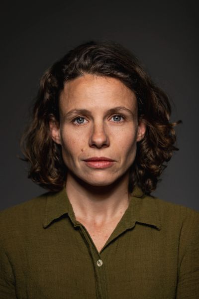 Mulher com expressão neutra de cabelo cacheado curto.