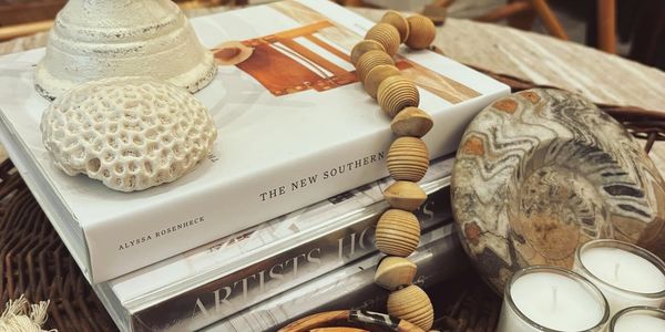 A group of decorative items: books, coral, beads, candles, and an Ammonite in a basket on a table. 