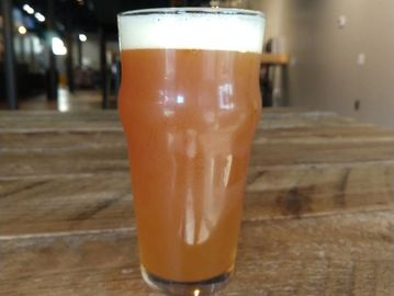 A pint glass filled with amber beer on a wooden table.