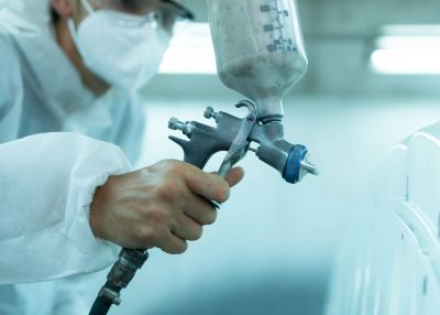 Person using a spray paint gun wearing protective gear.