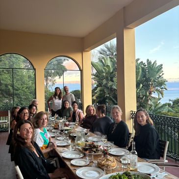 Group of people enjoying a meal on a covered terrace with a scenic view.