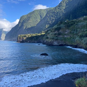 Coastal cliffs with lush greenery beside a calm blue sea under a clear sky.