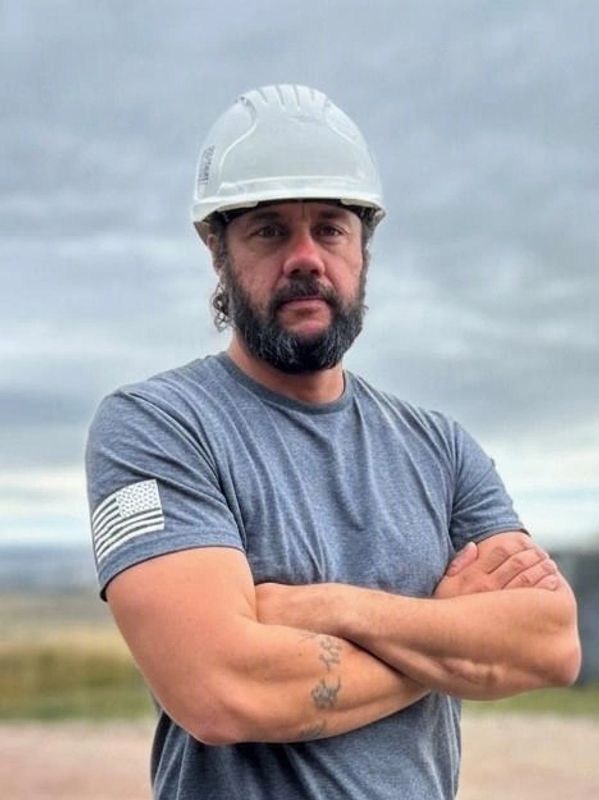 Man in a gray t-shirt and white safety helmet crossing his arms.