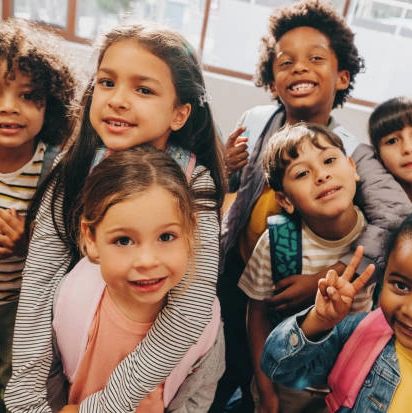 A group of smiling schoolchildren wearing backpacks indoors.