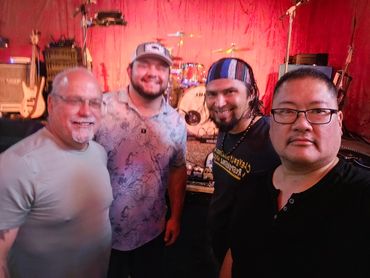 Four men posing in front of a stage with musical instruments.