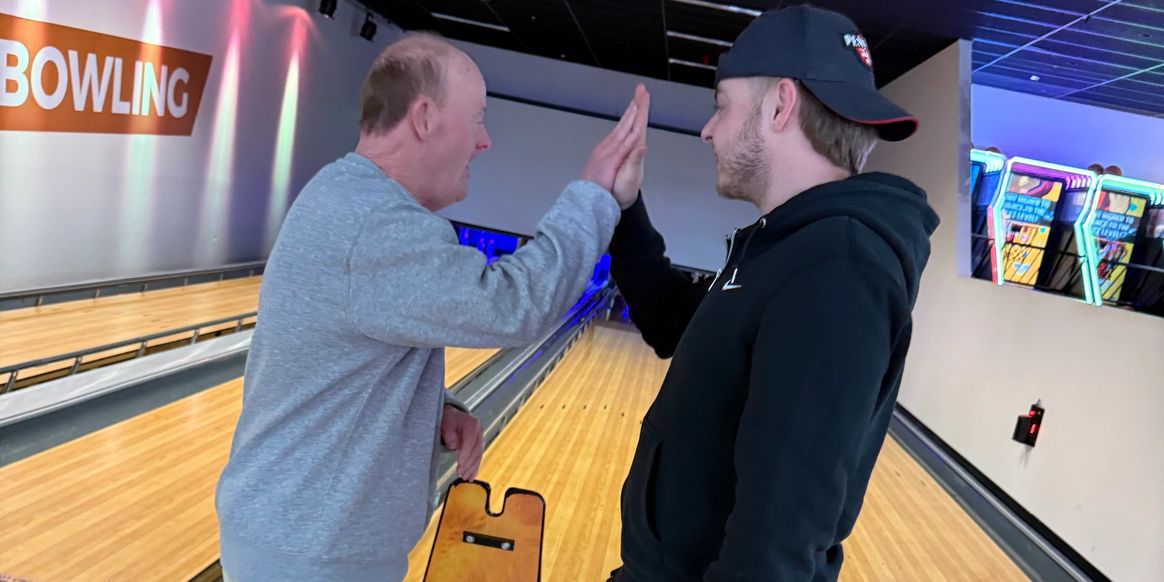 Two men high-five at a bowling alley near the lanes